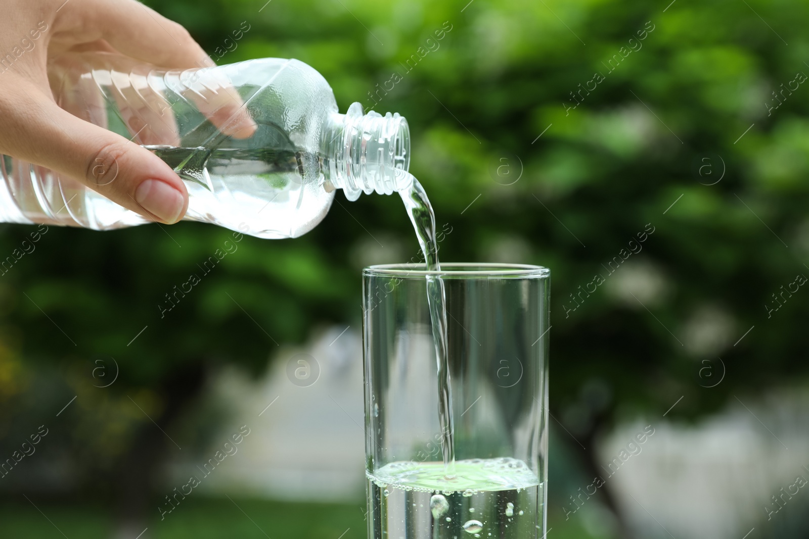 Photo of Woman pouring water from bottle into glass outdoors, closeup