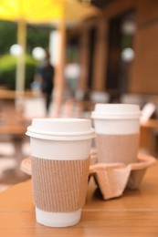 Photo of Takeaway paper coffee cups with plastic lids, sleeves and cardboard holder on wooden table outdoors