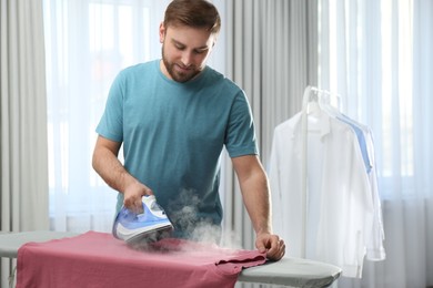 Photo of Young man ironing clean shirt at home