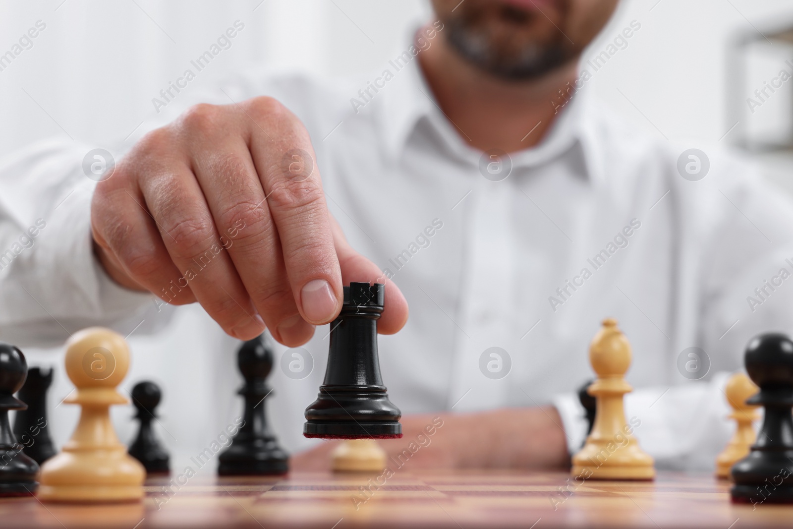 Photo of Man with rook game piece playing chess at checkerboard indoors, closeup
