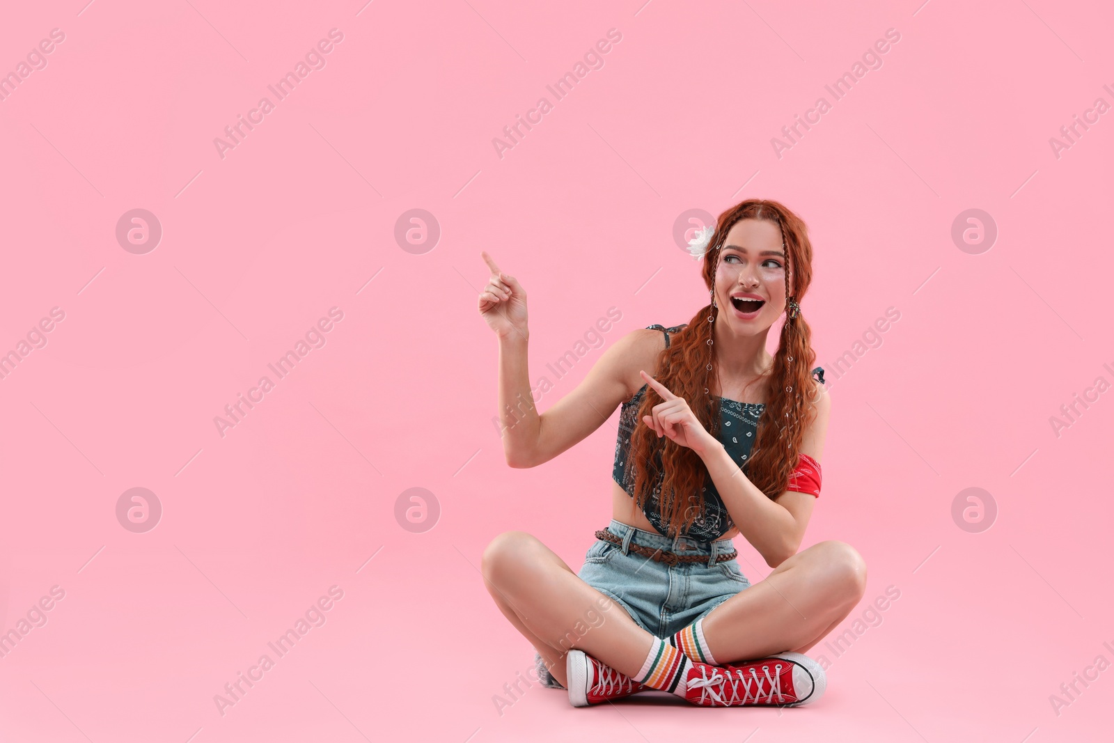 Photo of Beautiful young hippie woman pointing at something on pink background, space for text