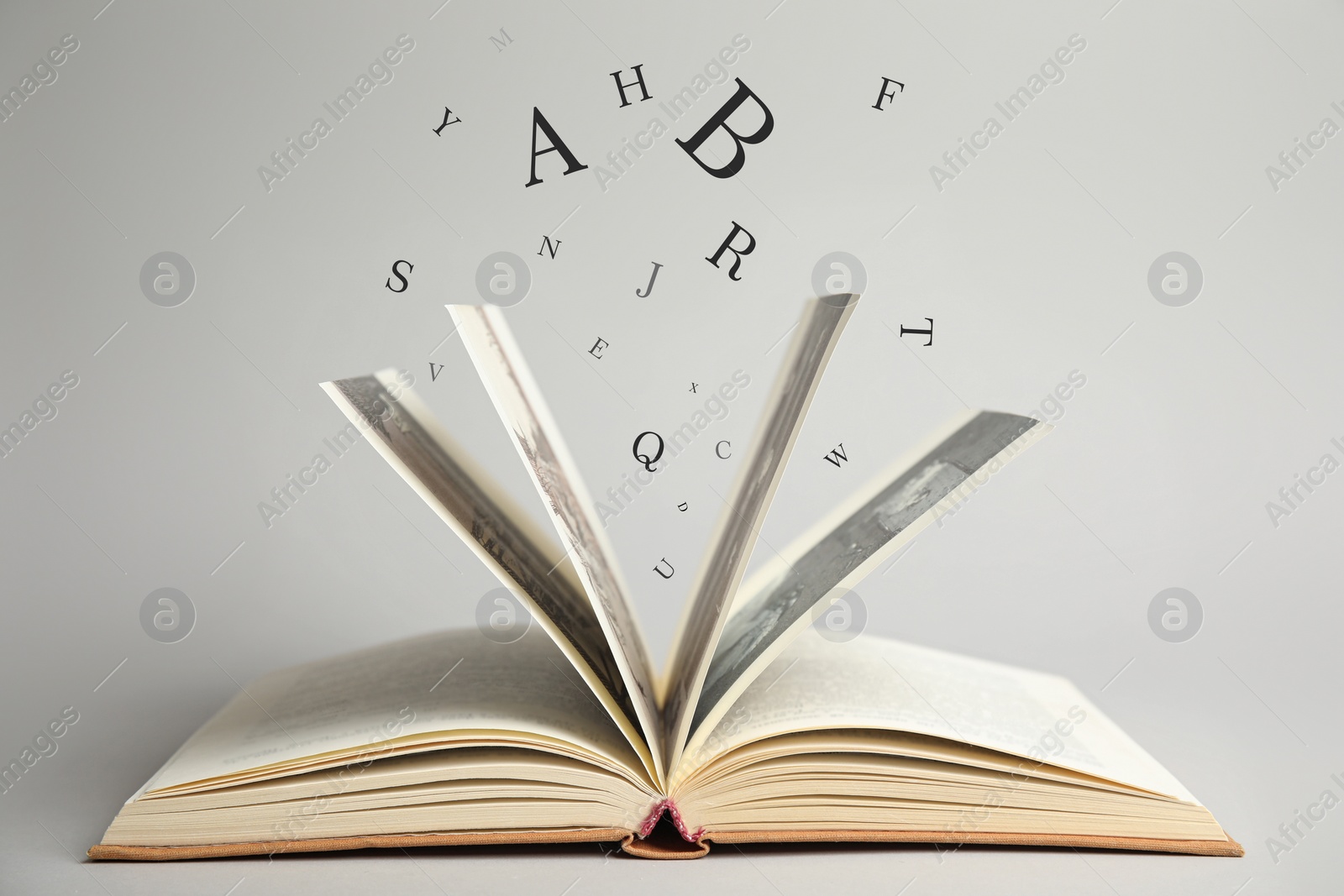 Image of Open book with letters flying out of it on light background