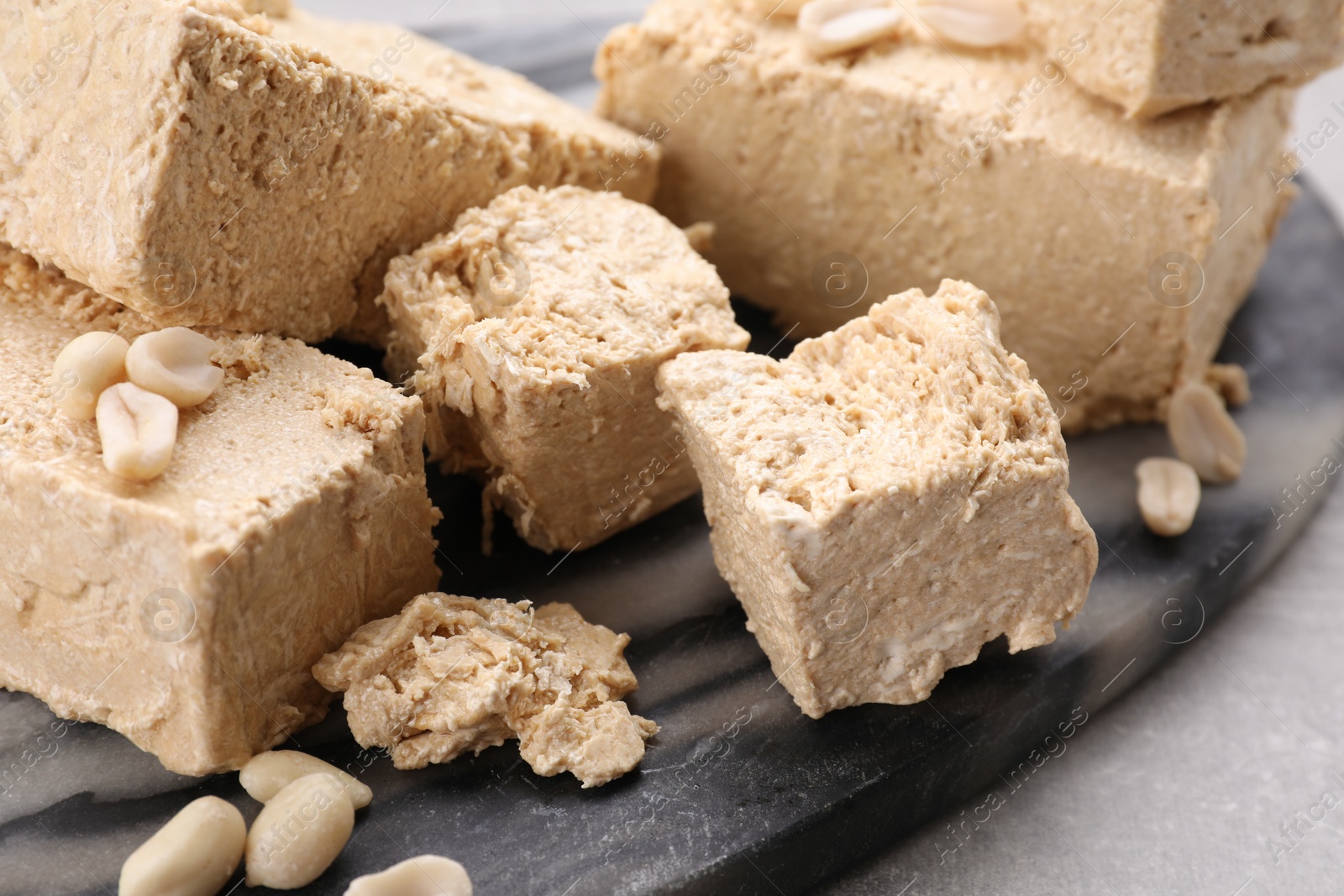 Photo of Pieces of tasty halva on dark gray marble board, closeup