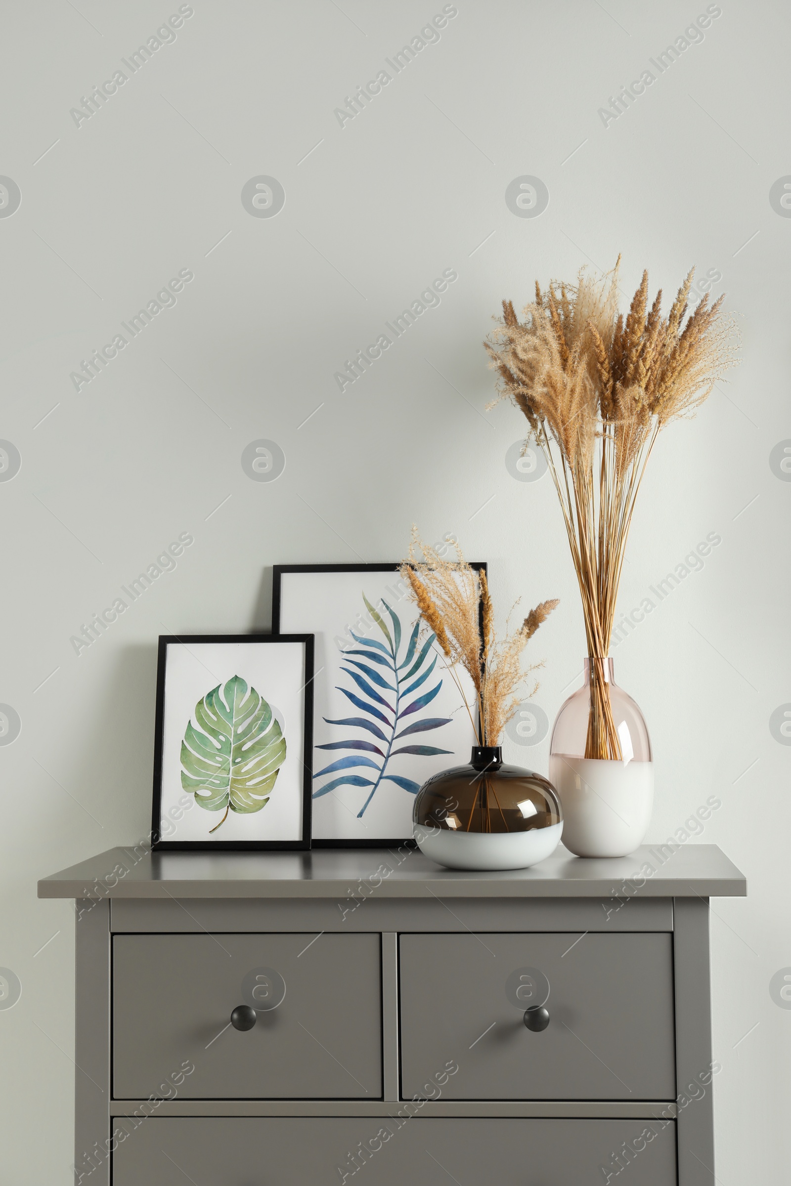 Photo of Reed's blossom in glass vases and pictures on grey cabinet indoors