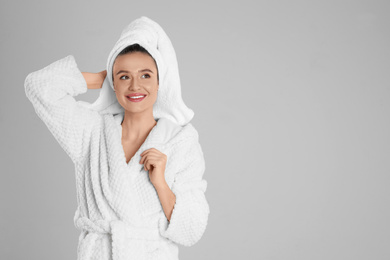 Beautiful young woman in bathrobe on light grey background. Space for text