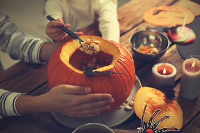 Photo of Mother and daughter making pumpkin jack o'lantern at wooden table, closeup. Halloween celebration