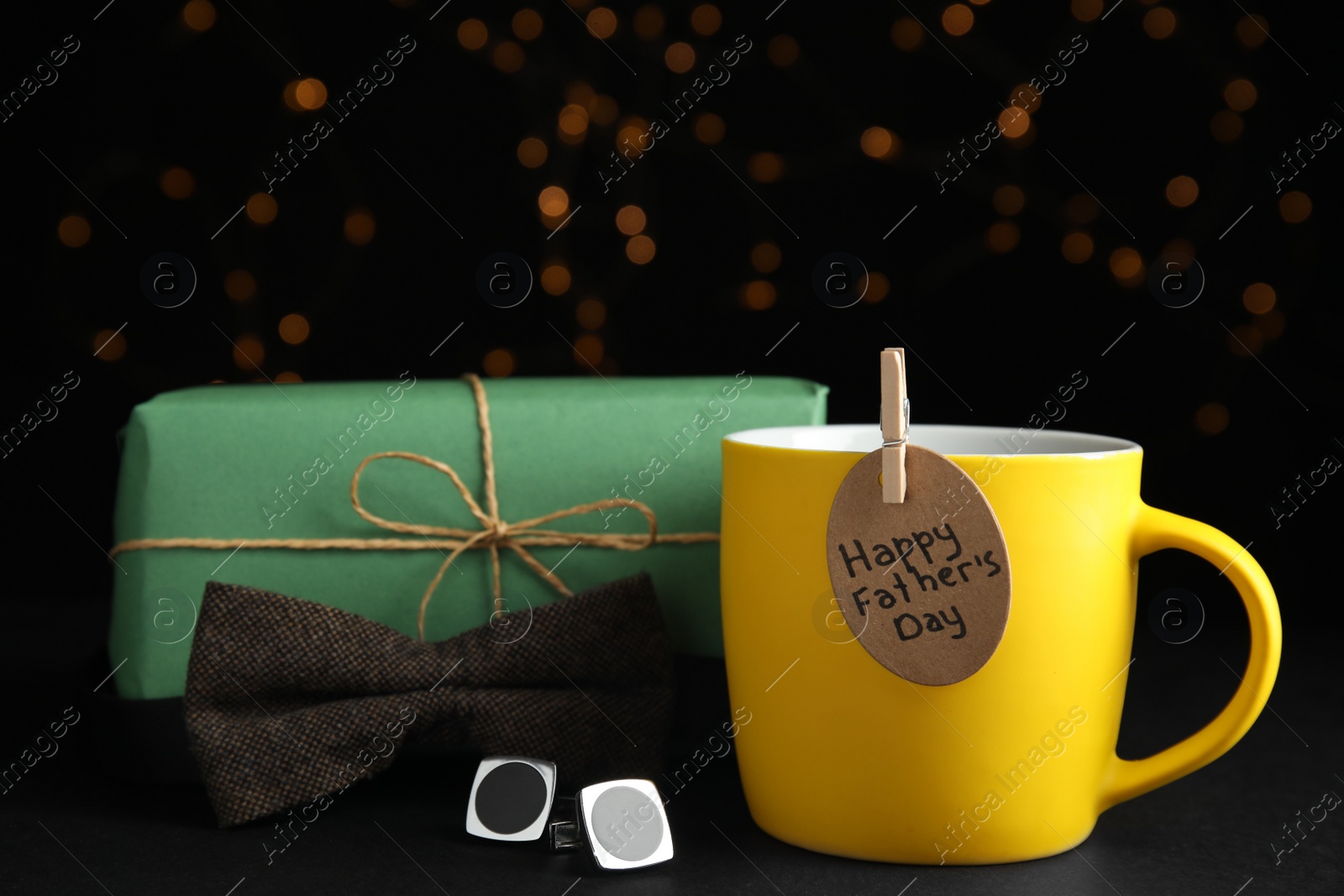 Photo of Composition with cup of drink and tag HAPPY FATHER'S DAY on black table against blurred lights