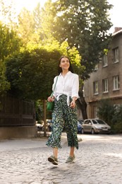 Beautiful young woman in stylish outfit walking on city street