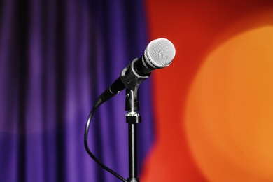 Photo of Stand with microphone on color background. Blurred lights