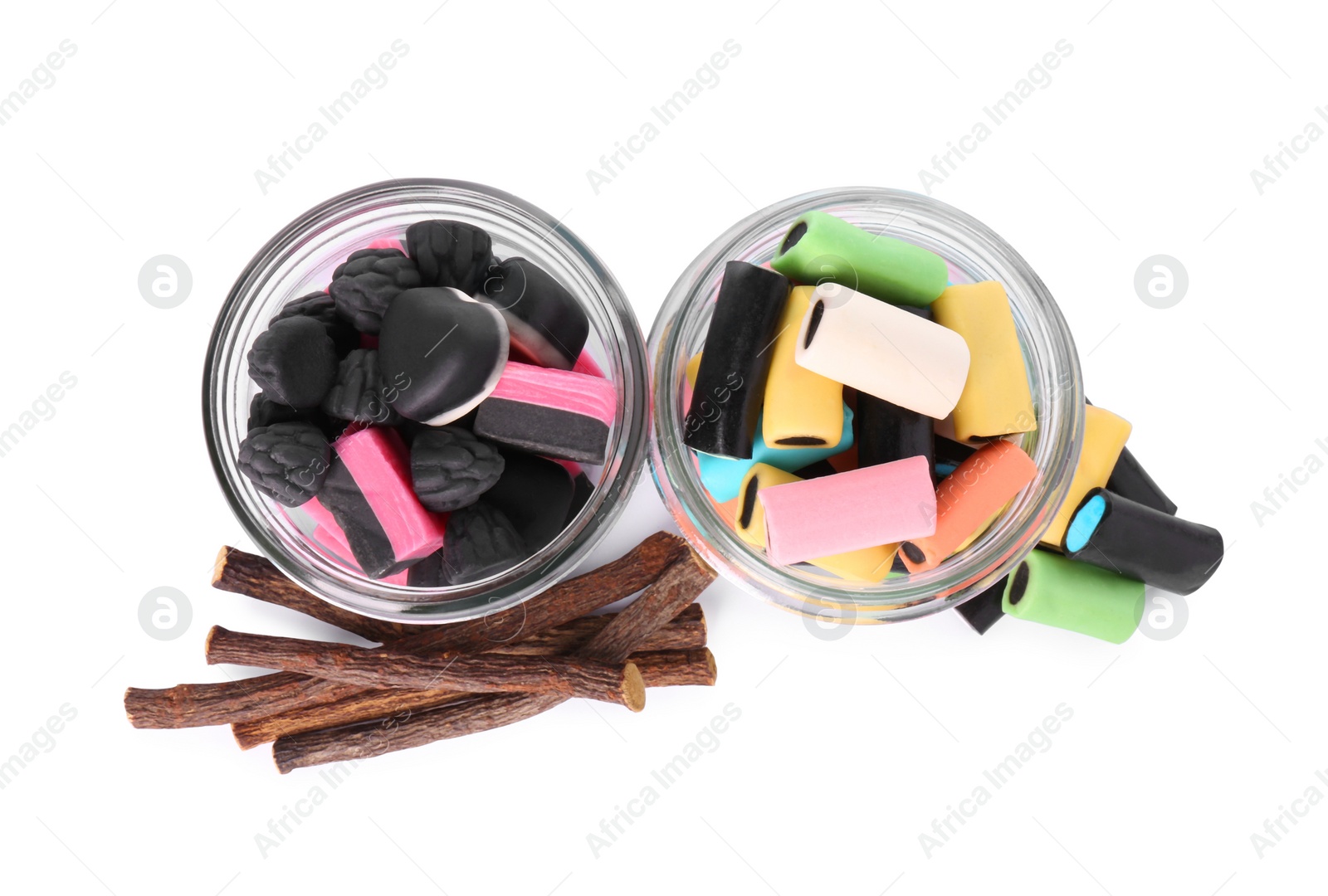 Photo of Glass jars of tasty candies and dried cut liquorice root isolated on white, top view