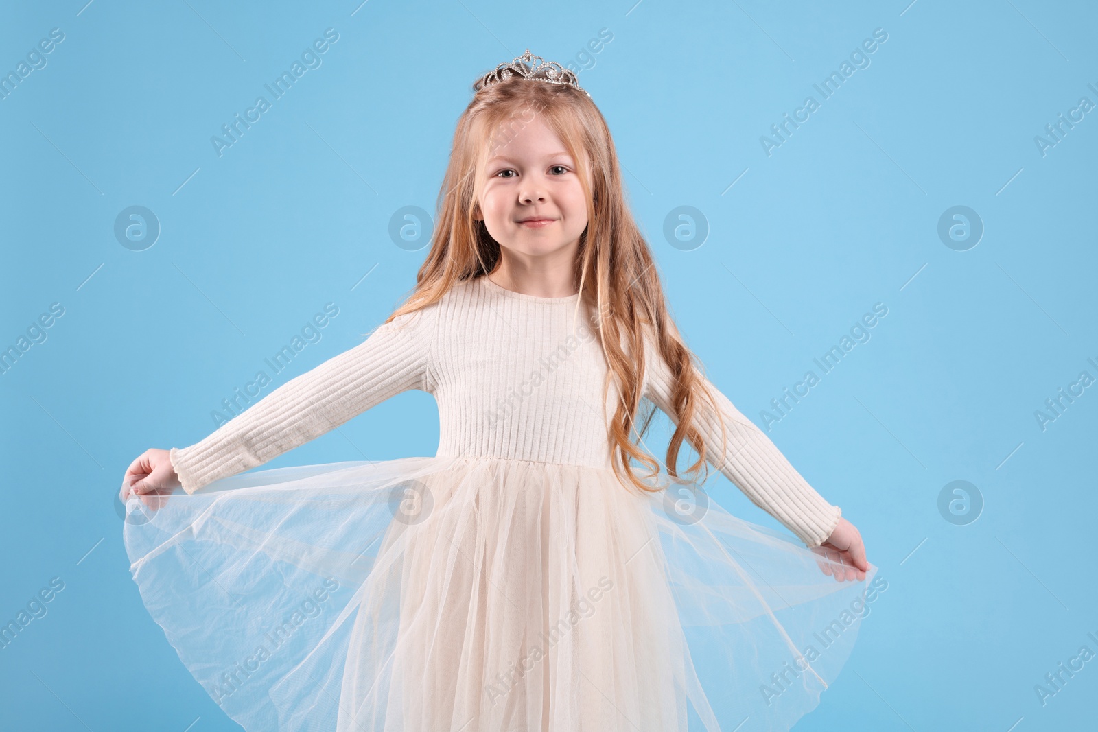 Photo of Cute girl in beautiful dress with diadem on light blue background. Little princess