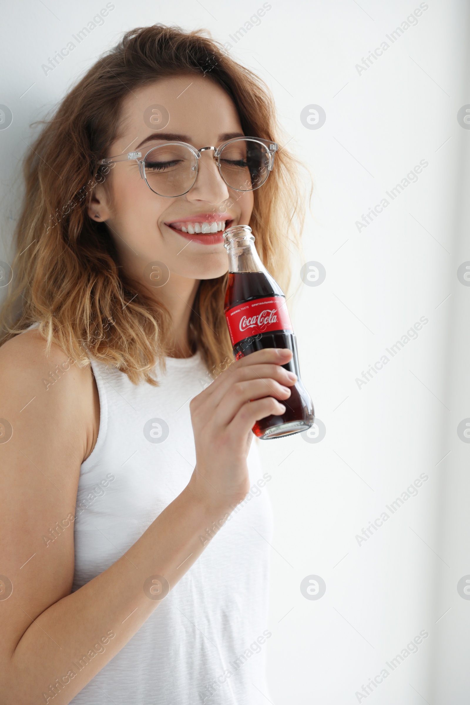 Photo of MYKOLAIV, UKRAINE - NOVEMBER 28, 2018: Young woman with bottle of Coca-Cola indoors