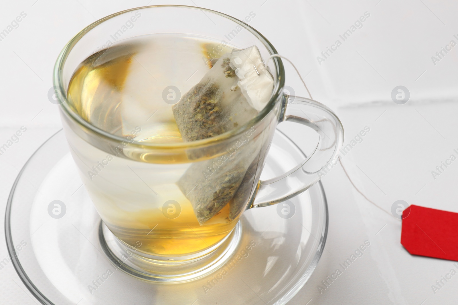 Photo of Tea bag in cup with hot drink on white table, closeup