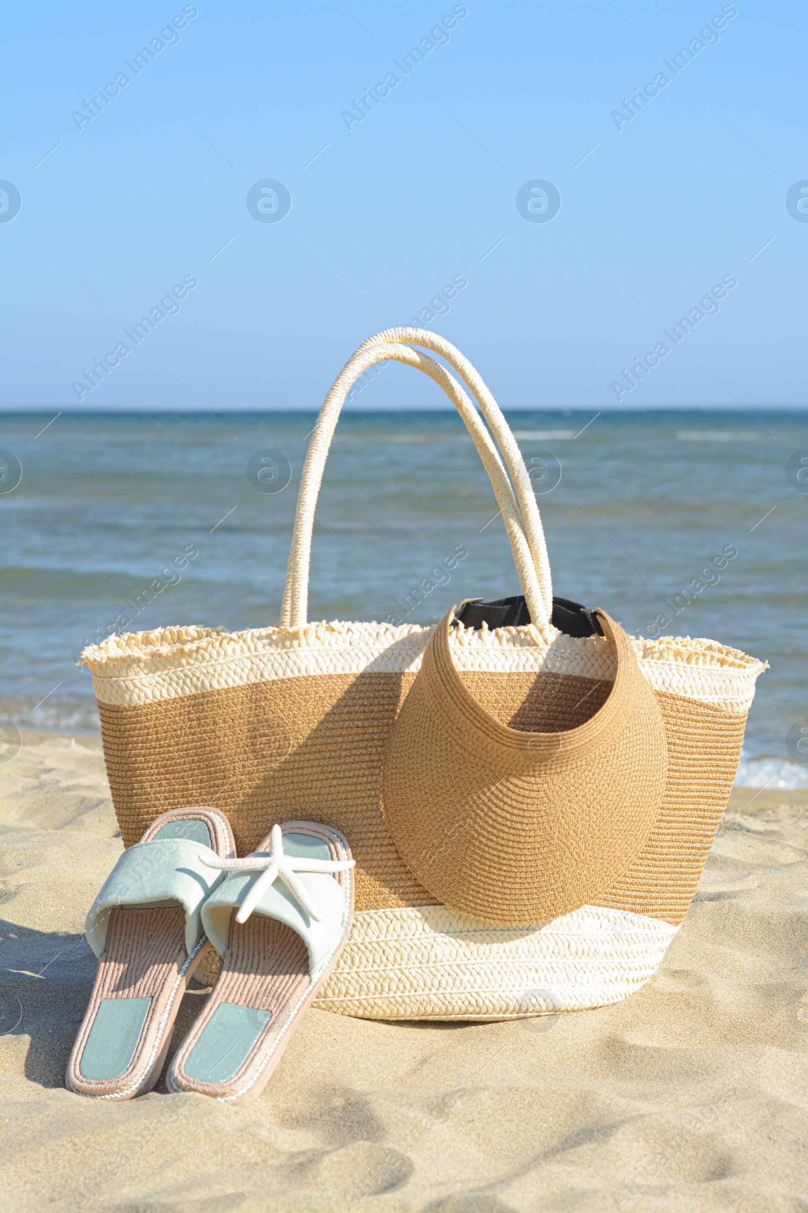 Photo of Stylish bag with slippers, visor cap and dry starfish on sandy beach near sea