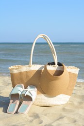 Stylish bag with slippers, visor cap and dry starfish on sandy beach near sea