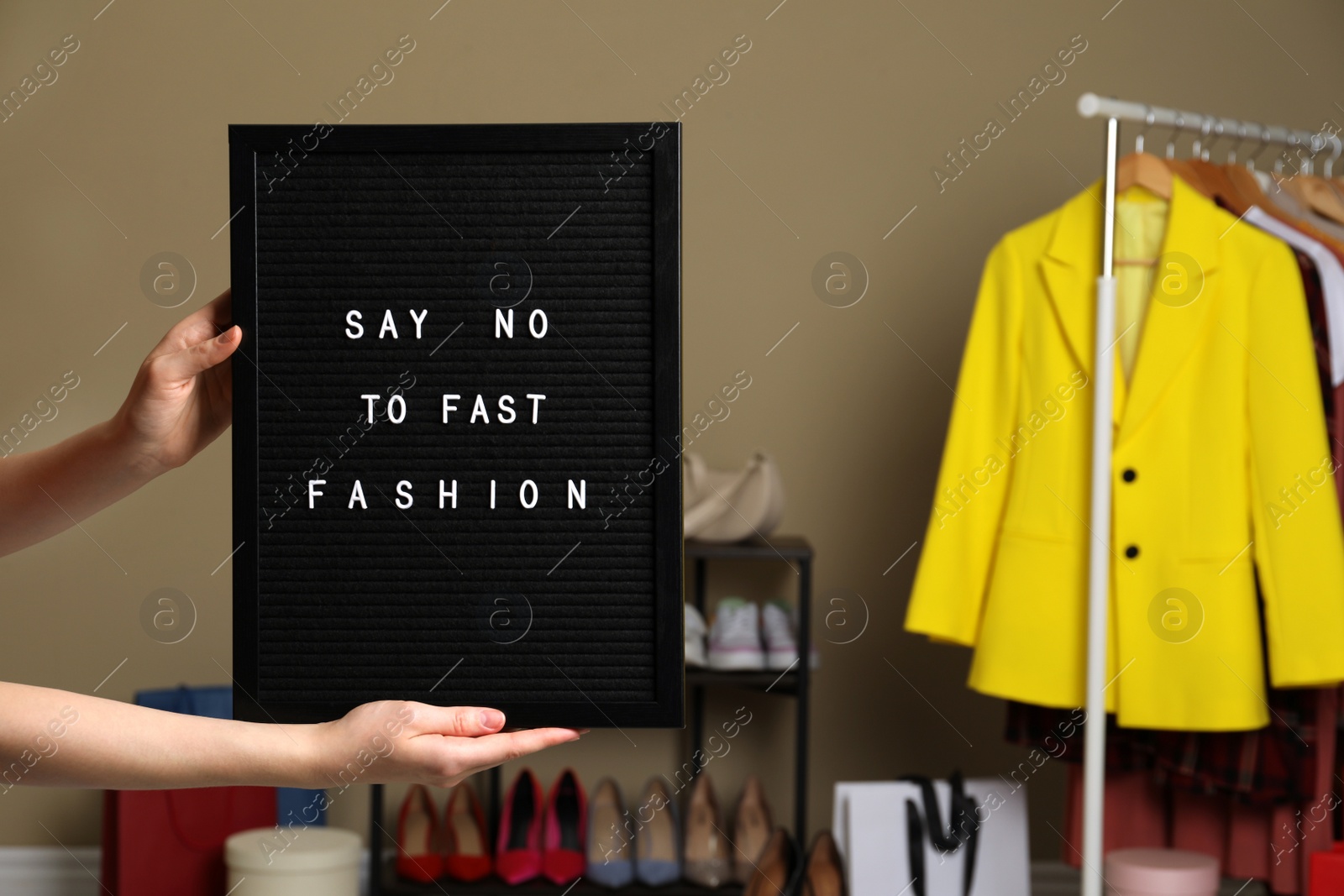 Photo of Woman holding black letter board with phrase SAY NO TO FAST FASHION indoors, closeup