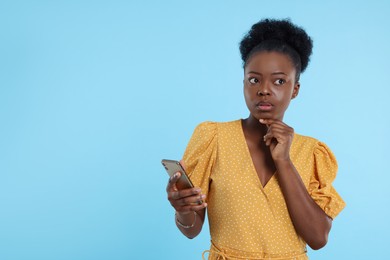 Photo of Concentrated young woman with smartphone on light blue background. Space for text