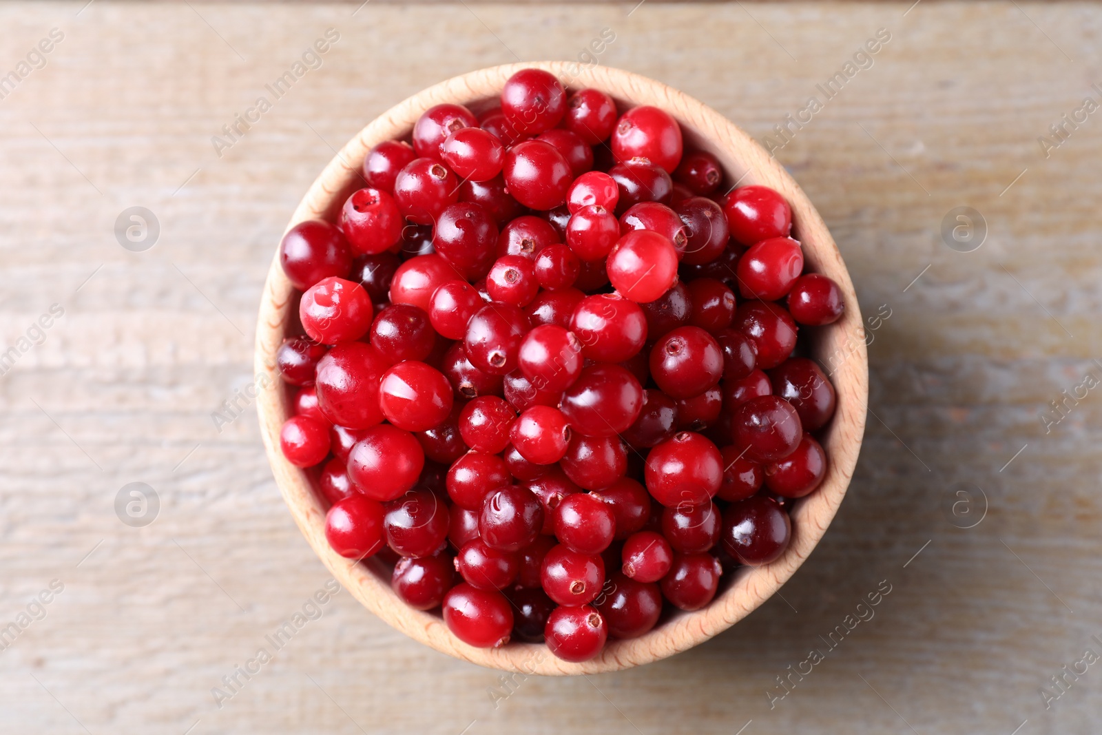 Photo of Fresh ripe cranberries in bowl on wooden table, top view