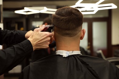 Professional hairdresser making stylish haircut in salon, back view