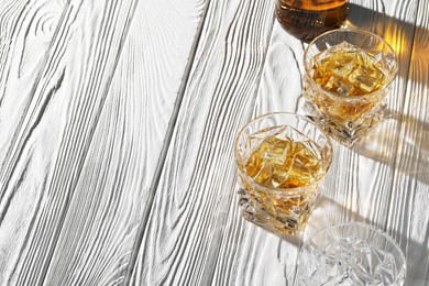 Whiskey with ice cubes in glasses on white wooden table, space for text