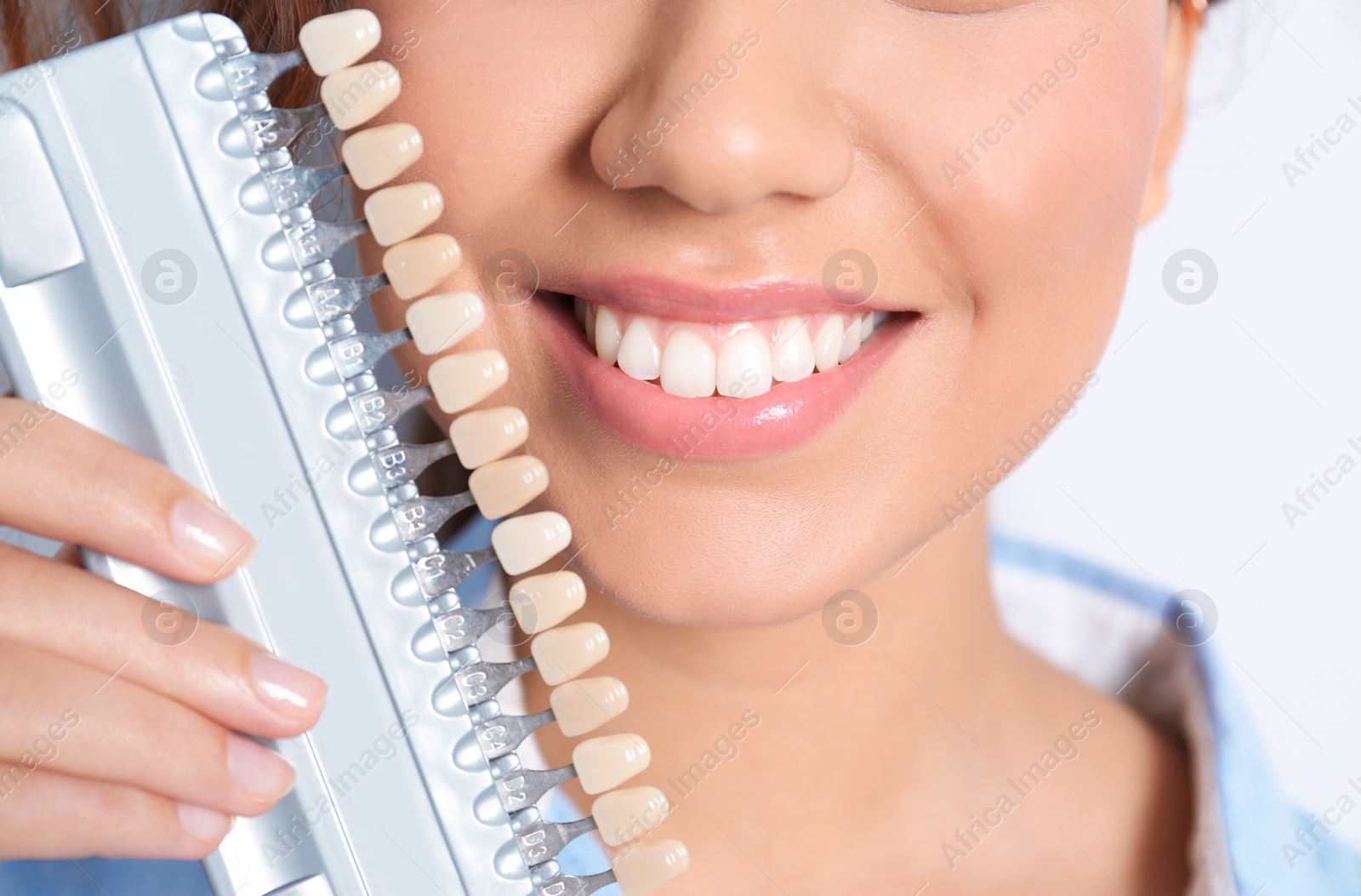 Photo of Young African-American woman with teeth color samples on light background, closeup