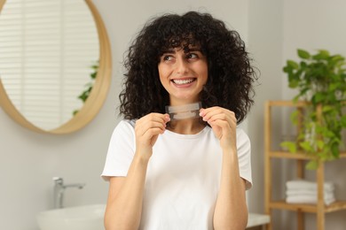 Photo of Young woman holding teeth whitening strips in bathroom