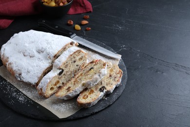 Photo of Traditional Christmas Stollen with icing sugar on black table, space for text
