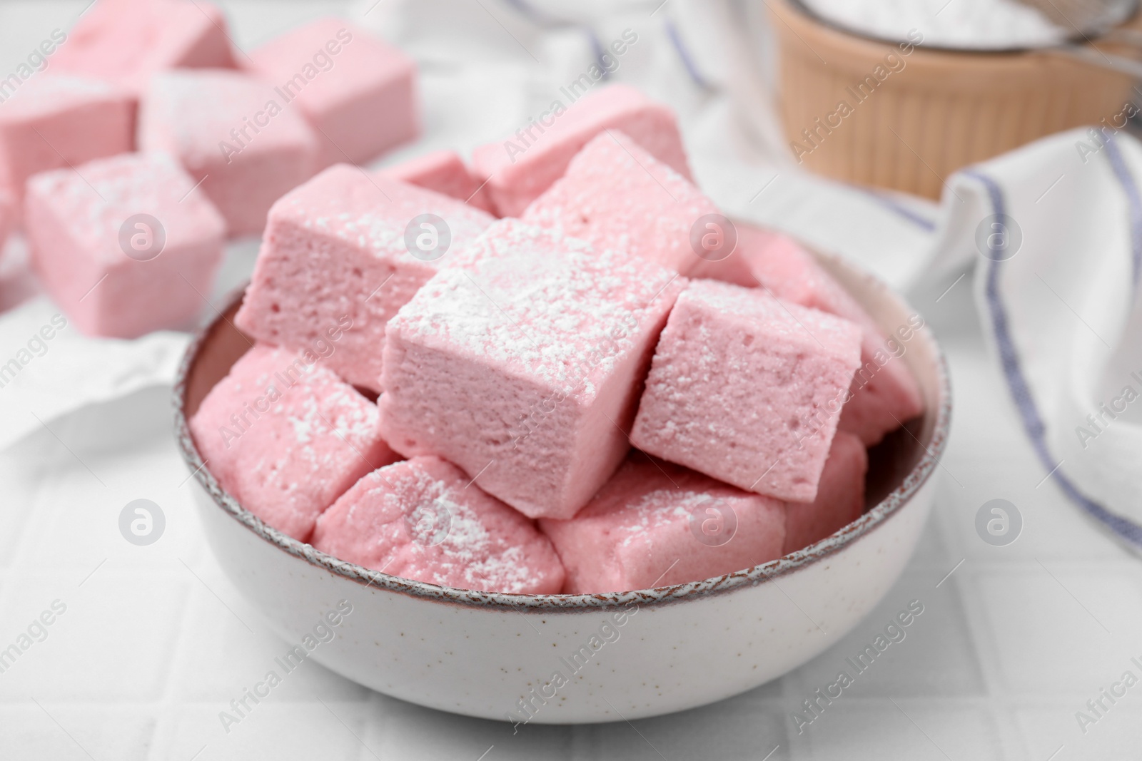 Photo of Bowl of delicious sweet marshmallows with powdered sugar on white table, closeup