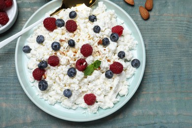 Photo of Delicious cottage cheese with fresh berries served for breakfast on light blue wooden table, flat lay