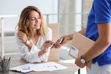 Photo of Woman using smartphone app to confirm receipt of envelope from courier in office