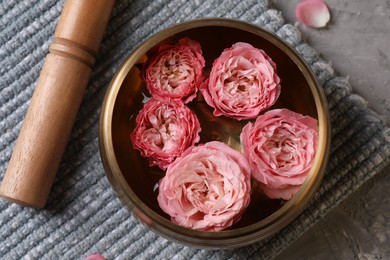 Photo of Tibetan singing bowl with water, beautiful roses and mallet on table, top view
