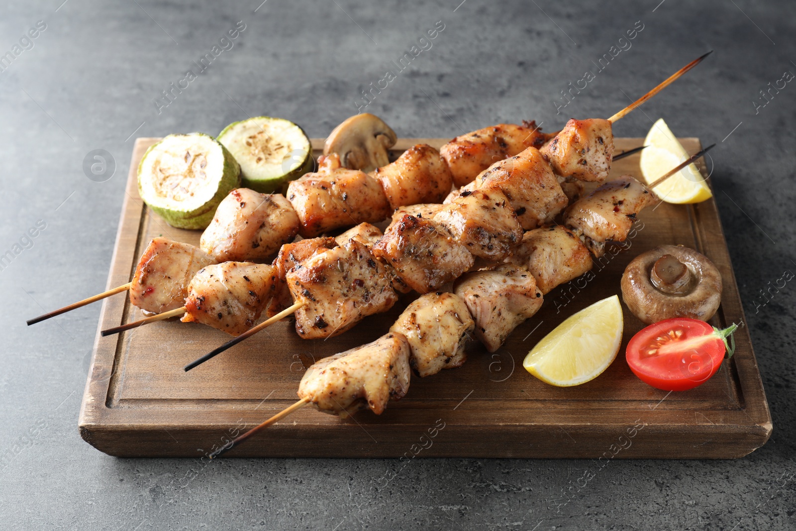 Photo of Delicious shish kebabs with vegetables and lemon on grey table