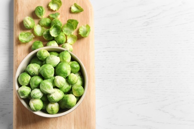 Board with bowl and Brussels sprouts on wooden background, top view. Space for text