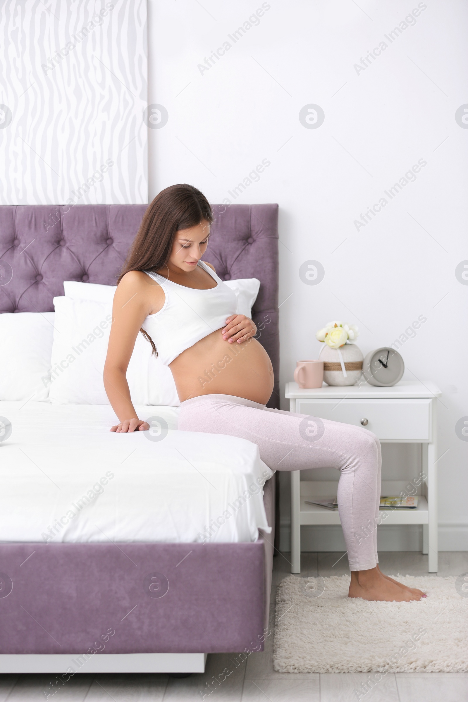 Photo of Happy pregnant woman sitting on bed at home