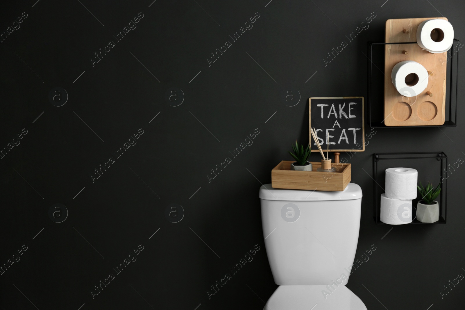 Photo of Decor elements, necessities and toilet bowl near black wall, space for text. Bathroom interior