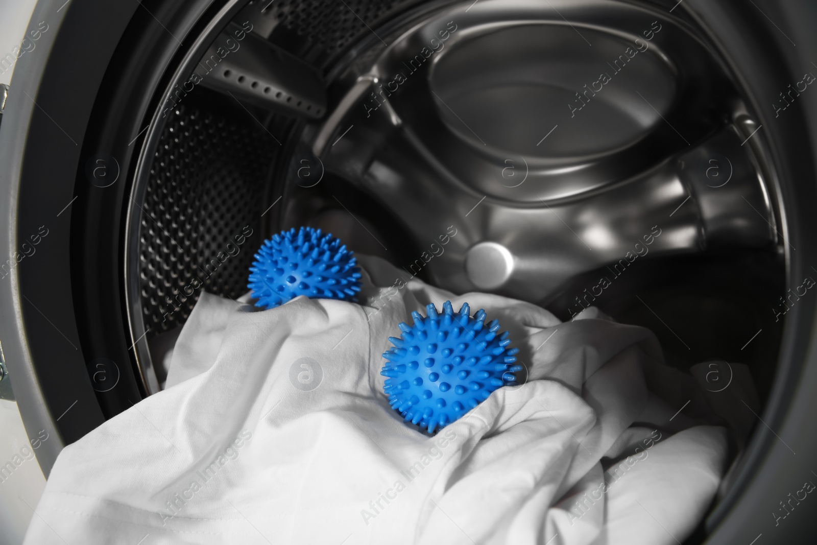 Photo of Blue dryer balls and clothes in washing machine drum, closeup