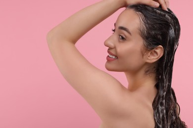 Beautiful happy woman washing hair on pink background. Space for text