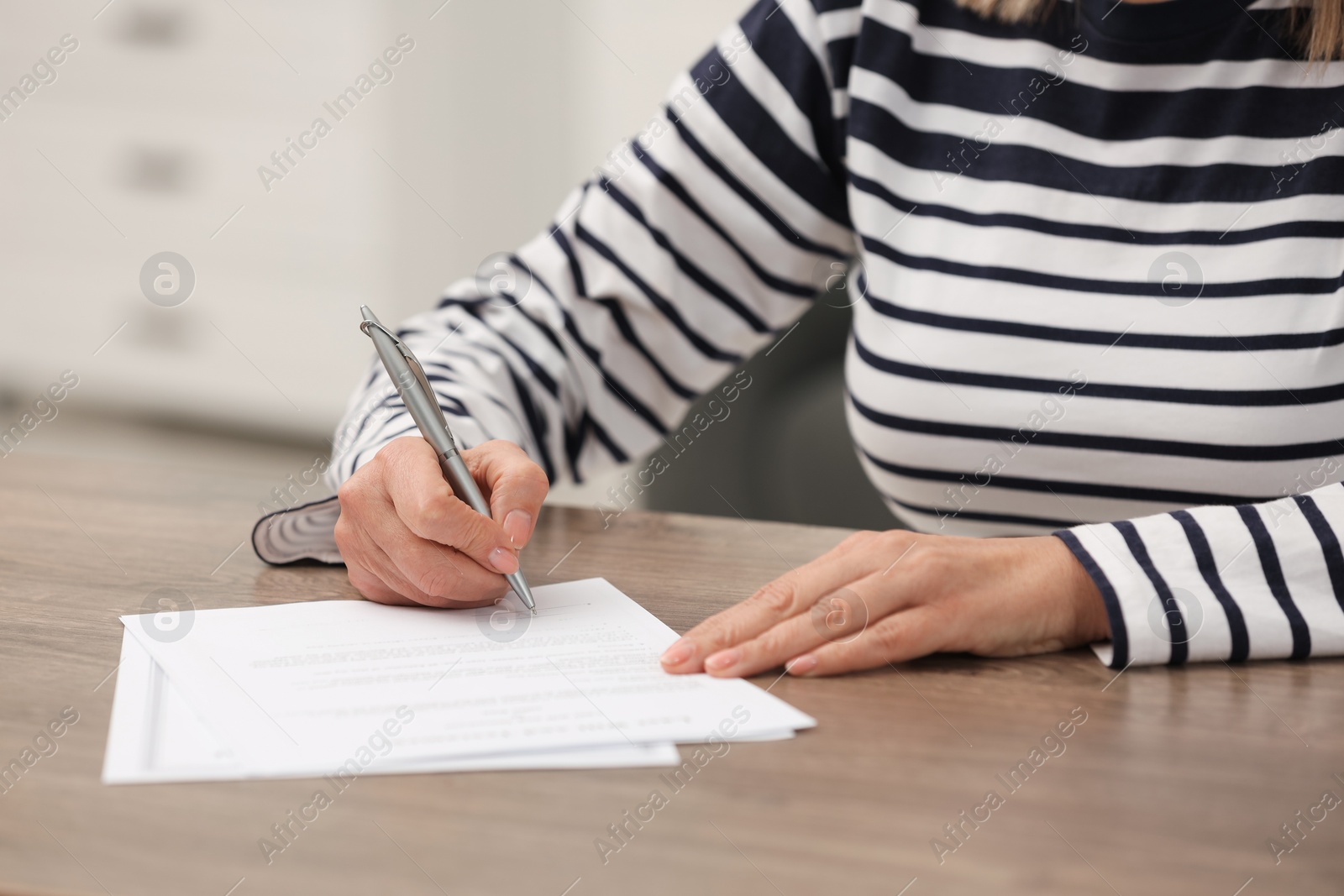 Photo of Senior woman signing Last Will and Testament at wooden table indoors, closeup