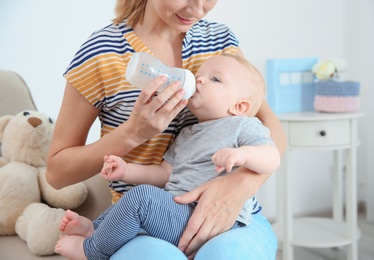Photo of Lovely mother feeding her baby from bottle in room at home