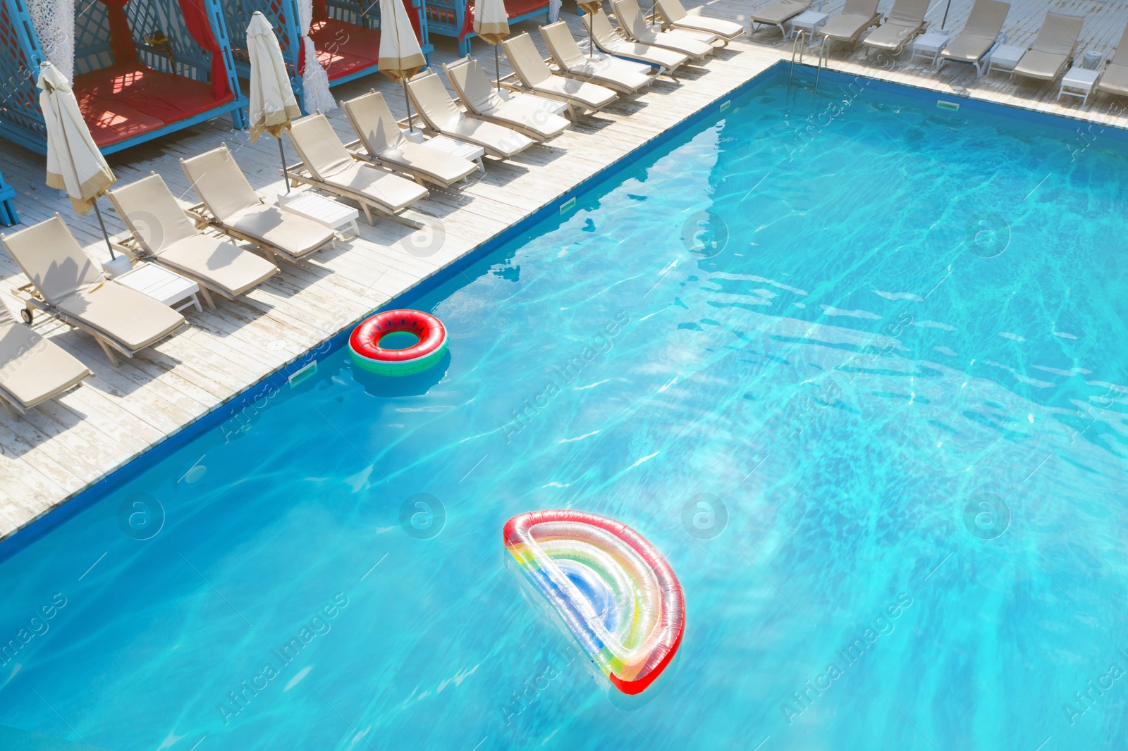 Image of Lounge chairs with umbrellas near swimming pool on sunny day 