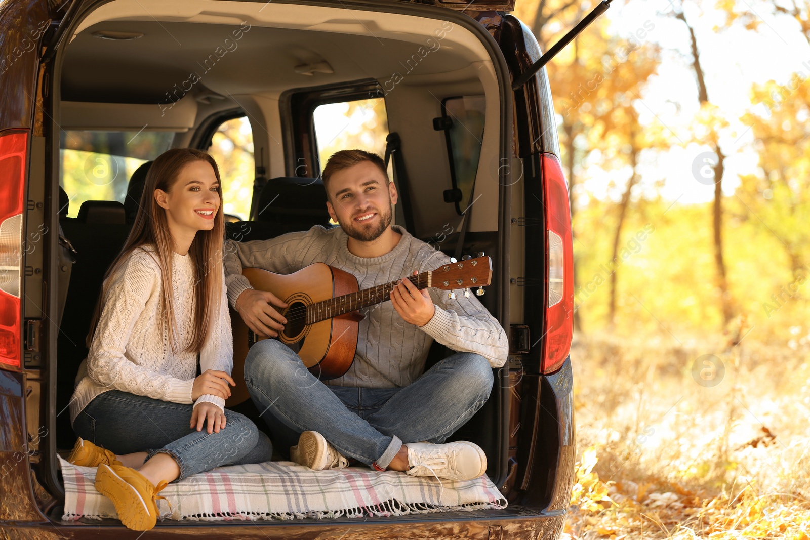 Photo of Young couple with guitar sitting in open car trunk outdoors