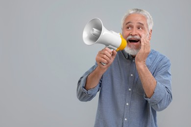 Photo of Special promotion. Senior man shouting in megaphone on light grey background. Space for text