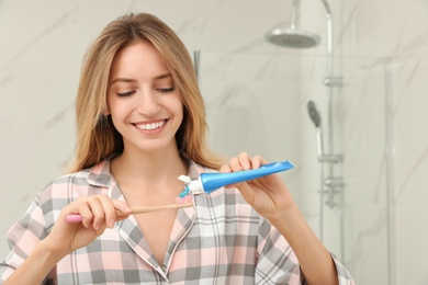 Photo of Woman applying toothpaste on brush in bathroom