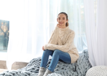 Photo of Beautiful teenage girl in warm cozy sweater sitting near window at home