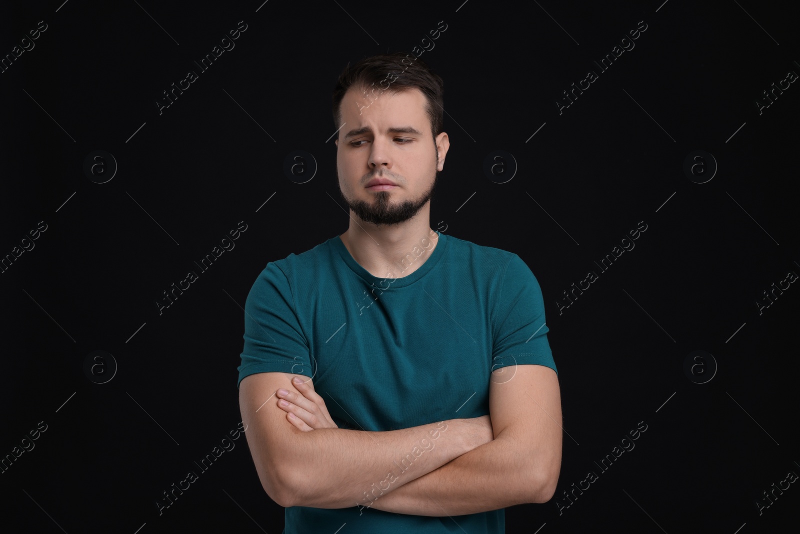 Photo of Portrait of sad man with crossed arms on black background