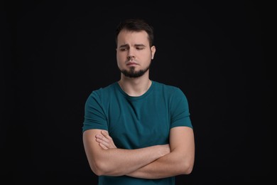 Photo of Portrait of sad man with crossed arms on black background