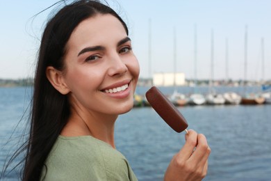 Photo of Beautiful young woman holding ice cream glazed in chocolate near river