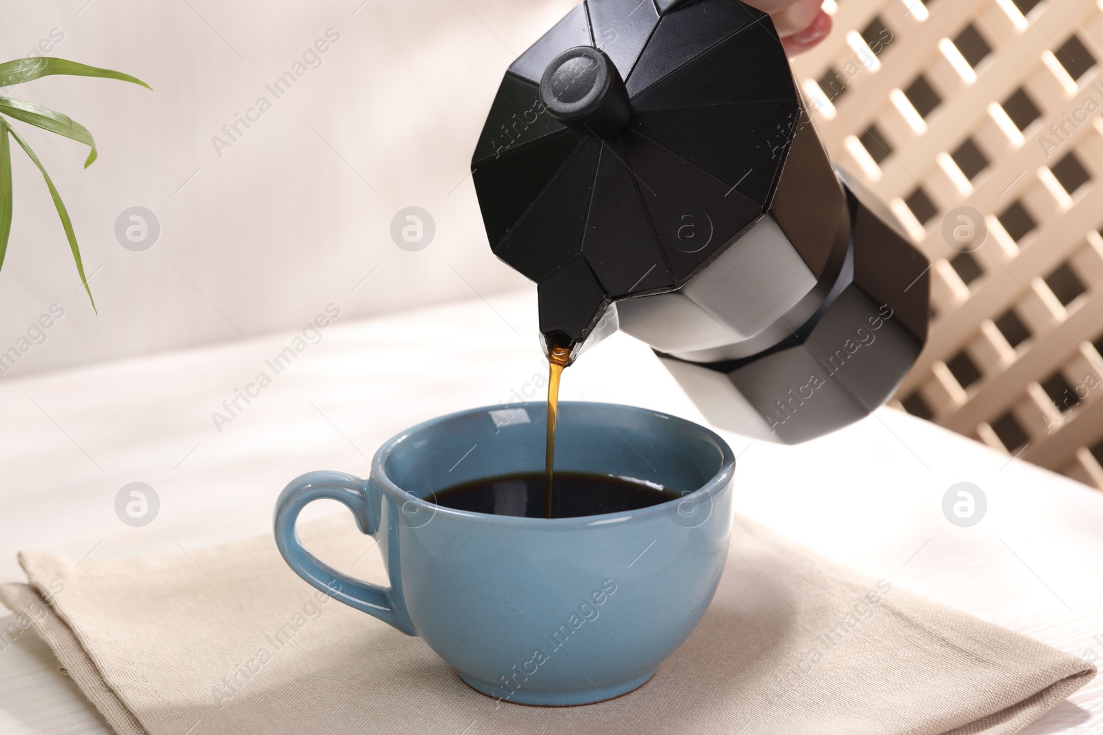 Photo of Pouring aromatic coffee from moka pot into cup at white table, closeup