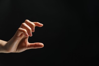 Woman holding something in hand on black background, closeup. Space for text