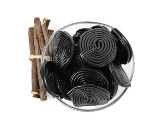 Tasty black candies and dried sticks of liquorice root on white background, top view